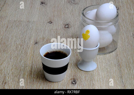 Kaffee und gekochtes Ei zu Ostern Frühstück auf Holztisch mit Eier im Glas Glas im Hintergrund Stockfoto