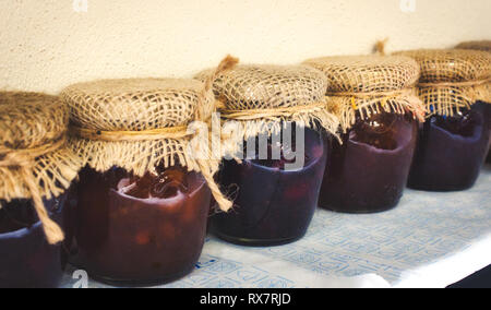 Glas Gläser vielfältige Marmeladen bedeckt mit Sack und mit String in einer Reihe auf einem Regal gebunden Stockfoto