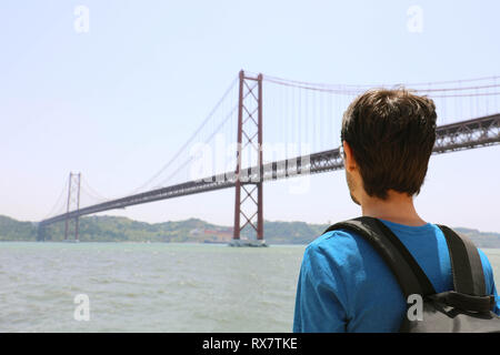 Zurück Blick auf junge Backpacker Mann an der Brücke suchen. Geschäftsreisende oder Touristen mit Rucksack auf der Uferpromenade in Lissabon Portugal am 25. April Stockfoto