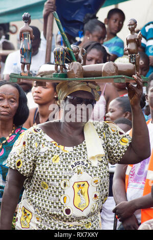 Bassam, Côte d'Ivoire - November 7, 2015: möchte Frau in Schwarz Gläser und Schal auf dem Kopf, lädt einen Fach mit Status folgt ihre Kollegen Stockfoto