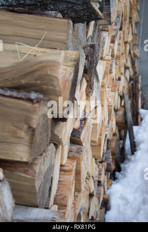 Stamm im Schnee im Winter bedeckt, im Freien gestapelt industrielle Holz Material, Stapel von Rundholz. Vorbereitung von Brennholz für den Winter. Stockfoto