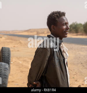Kerma, Sudan, Februar 8., 2019: Junge Sudanesische lächelnden Mann in seitlichen Profil auf dem Weg durch die Wüste im Norden des Sudan mit alten, abgenutzten Leder jac Stockfoto
