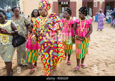 Bassam, Côte d'Ivoire - November 7, 2015: Die Queen in der traditionellen loincloths, Armband, Ohrringe und Halsketten Gold gekleidet ist durch wenig begleitet Stockfoto