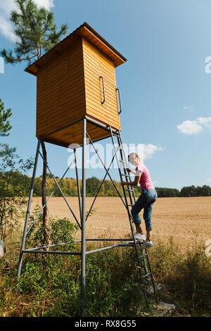 Frau klettern auf hohen Sitz für Jäger mit Stahl und Holz. Sonnigen Tag. Stockfoto