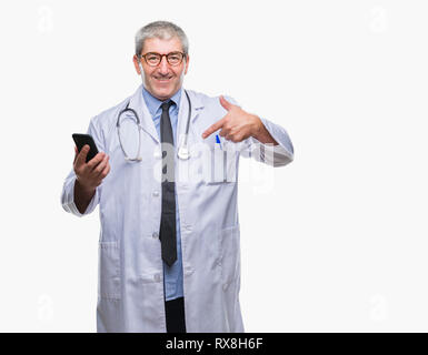 Stattliche leitender Arzt Mann sms senden Nachricht mit Smartphone über isolierte Hintergrund mit Überraschung Gesicht zeigenden Finger zu sich selbst Stockfoto