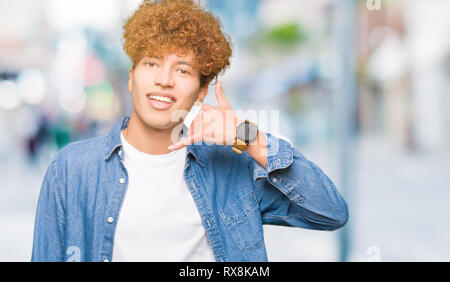 Junger stattlicher Mann mit afro Haar Jeansjacke lächelnd tun Telefon Geste mit der Hand und der Finger wie im Gespräch am Telefon. Kommunikation Stockfoto