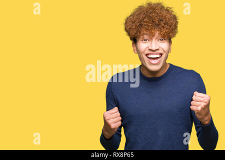 Junger stattlicher Mann mit afro Haar sehr glücklich und aufgeregt, Sieger Geste mit erhobenen Armen, lächelnd und Schreien für den Erfolg. Feier Konzept Stockfoto