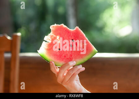 Woman holding Stück frischen leckeren organischen Wassermelone berry sitzen auf hölzernen Terrasse. Person auf Picknick im Freien mit saftigen reife rote Melone Berry im Stockfoto