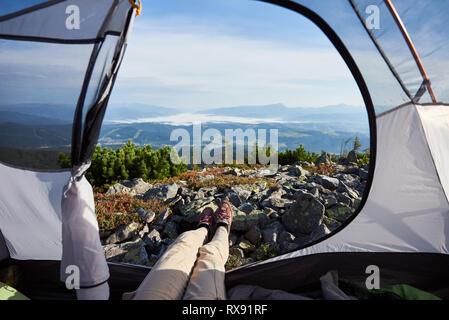 Camping auf der Spitze des Berges, auf Sommermorgen. Junge camper Frau im Eingang der touristischen Zelt sitzen. Ansicht von innen ein Zelt auf schönen Nebel Stockfoto