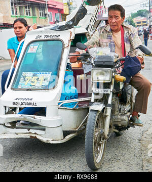 Roxas City, Capiz Provinz, Philippinen: Low-angle Ansicht eines vorbeifahrenden alten Dreirad mit einem männlichen und weiblichen Passagier und Fracht Stockfoto