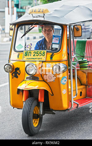 Bangkok, Thailand: Close-up Vorderansicht eines Gelb lackiert Tuk-tuk mit einem mittlerem Alter männliche Fahrer, von dem übrigen Datenverkehr isoliert Stockfoto