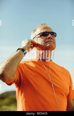 Close up Portrait eines älteren Mannes in dunklen Brillen stehen draußen und weg schauen. Mann Hören von Musik über Kopfhörer. Stockfoto