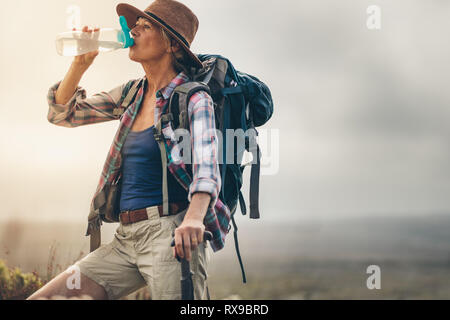 Nahaufnahme eines älteren weiblichen Wanderer eine Pause während ihrer Wanderung und Trinkwasser. Seitenansicht einer Frau Wanderer mit Rucksack und Hut trinken ... Stockfoto