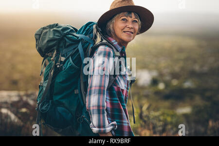 Nahaufnahme von einer älteren Frau mit Hut und Rucksack auf einen Urlaub. Seitenansicht eines weiblichen Wanderer auf einem Hügel während Ihrer Wanderung. Stockfoto