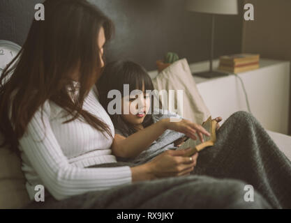 Mutter und Tochter lesen Buch zu Hause im Schlafzimmer Stockfoto