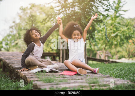 Wenig Afro kind Mädchen lesen Buch zwischen grünen Spitzen wiese Garten mit Freund und Hand zusammen Stockfoto