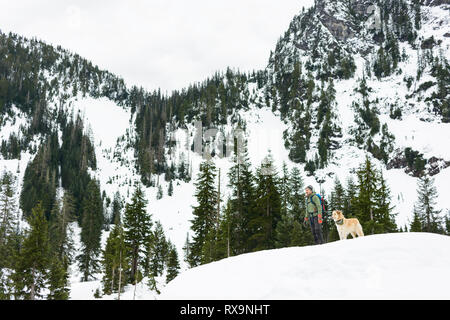 Low Angle View männlicher Wanderer mit Hund stehend auf schneebedeckten Feld gegen Berg Stockfoto