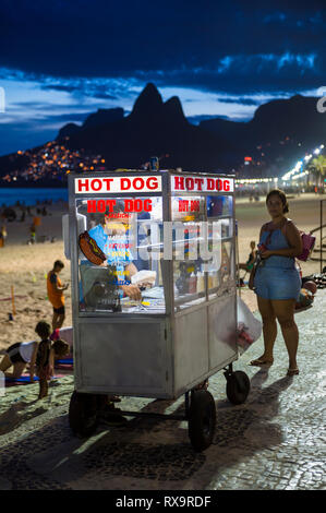 RIO DE JANEIRO - Februar 10, 2017: Ein Kunde steht warten als Verkäufer ihre Bestellung bereitet auf eine mobile Hot Dog cart auf den Ipanema Beach Boardwalk. Stockfoto