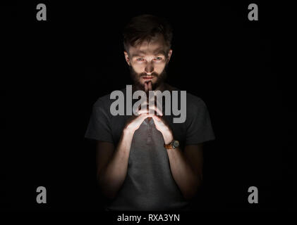 Portrait von zuversichtlich nachdenklicher Mann mit Bart steht auf schwarzem Hintergrund Stockfoto
