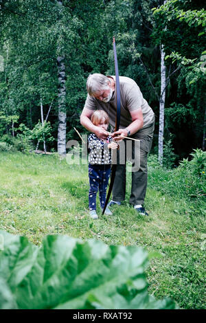 Großvater guiding Enkelin in dem Ziel, Pfeil beim Stehen auf Wiese am Wald Stockfoto