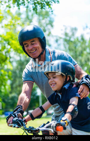 Älterer Mann sein Enkel hilft mit Fahrrad Stockfoto