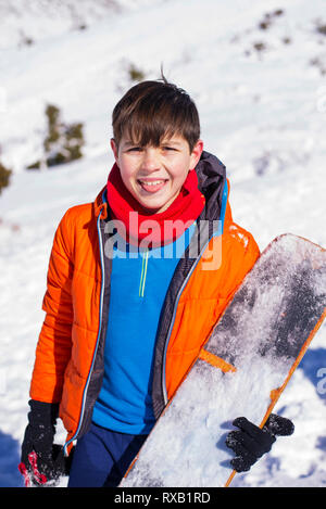 Porträt der Jungen heraus haften Zunge halten Snowboard auf schneebedeckte Berge im Winter Stockfoto