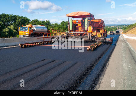 Rückansicht eines Fertiger, fertiger Estrich und Steuerung. Vordergrund Titel links von der Tire Walzenpressen beim Verdichten Asphalt. Stockfoto