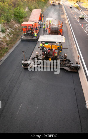 Asphalt Anwendung auf einer Schnellstraße. Alle Geräte in Aktion asphalt Lkw, transfer vehicle, Straßenfertiger. nach oben Blick auf die Bohle Stockfoto