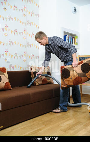 Der Mann reinigt die Zimmer. Er säubert das Sofa mit einem Staubsauger. Stockfoto