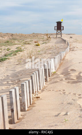 Sandstrand mit Bademeister Turm in der Ferne. Reihe von zufälligen Holz- Beiträge führen zu den oben geschlossen Turm Stockfoto