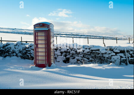 Traditionelles rotes BT Telefonzelle in ländlicher Lage auf einem winterlichen, verschneiten Tag Stockfoto