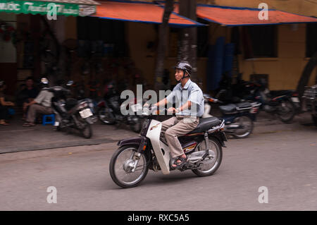 Eine vietnamesische Mann Reiten auf einem Motorrad entlang einer Straße, Hanoi, Vietnam Stockfoto