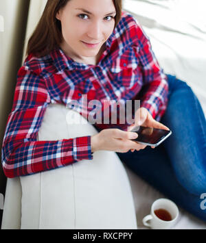Junge Frau mit Handy zu Hause sitzen auf dem Sofa entspannen Stockfoto