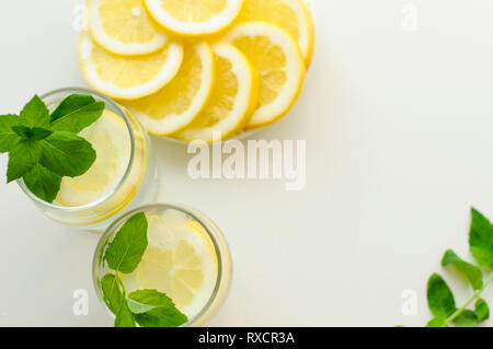 Blick von oben auf ein Arrangement mit erfrischenden Sommer Getränke in zwei Gläser, Teller voll von zitronenscheiben und frische Minze, alle auf Weiß Stockfoto