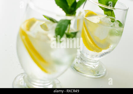 Zwei transparente Gläser mit erfrischenden und kalte Limonade mit Eiswürfel, Zitronenscheiben und Minzeblättchen. Stockfoto