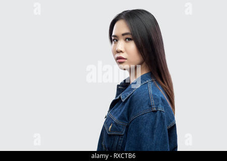 Profil Seitenansicht Portrait von Ruhe ernste schöne Brünette asiatische junge Frau in lässigem Blue Denim Jacke mit Make-up stehen und von der Kamera Stockfoto