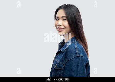 Profil Seitenansicht Portrait von glücklich schöne Brünette asiatischen Mädchen in lässigem Blue Denim Jacke mit Make-up toothy Lächeln und Kamera. Stockfoto