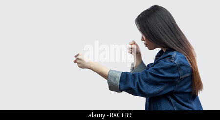 Profil Seitenansicht Portrait von schöne Brünette junge Frau in lässigem Blue Denim Jacke mit Make-up stehen in Boxen Fäuste Angriff oder Verteidigung. Pflege Stockfoto