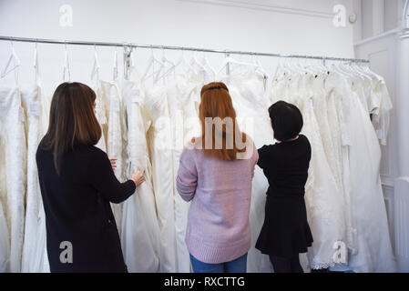 2 Verkäuferinnen helfen, eine hübsche rothaarige Mädchen ein Brautkleid zu wählen Stockfoto