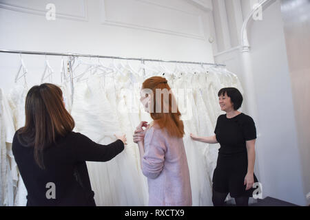 2 Verkäuferinnen helfen, eine hübsche rothaarige Mädchen ein Brautkleid zu wählen Stockfoto