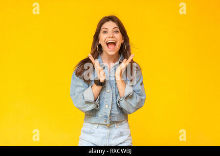 Portrait von überrascht schöne Brünette junge Frau mit Make-up in Denim lässige Stil stehen und an der Kamera mit offenen Mund und erstaunt. Stockfoto