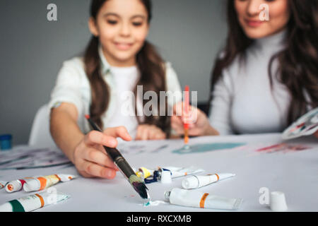 Schöne Brünette weißen Mutter und Tochter Farbe zusammen im Zimmer. Cut ansehen und unscharfes Bild. Happy girl, Pinsel in Farbe. Mutter sitzen Stockfoto