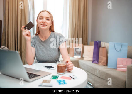 Online Shopping zu Hause. Junge Frau bereit ist, Geld von Payment Card am schwarzen Freitag zu verbringen, während am Tisch sitzen Stockfoto