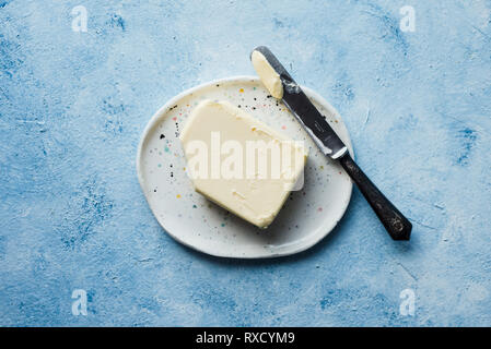 Block von Butter mit einem alten Messer auf einem handgearbeiteten Platte Stockfoto