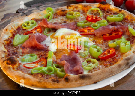 Pizza mit Tomatensoße, Schinken, Ei, frische grüne und rote Paprika, Gelb, Käse, Olivenöl und Oregano. Stockfoto