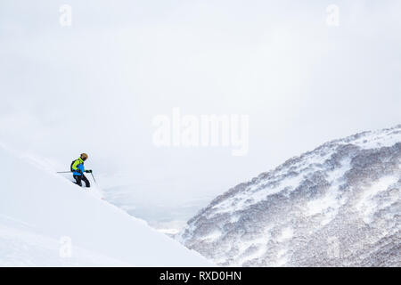 Telemark skier in Grün und Blau auf Pulver Hang mit Blick auf Niseko Mountain im Hinterland von Hokkaido, Japan. Stockfoto