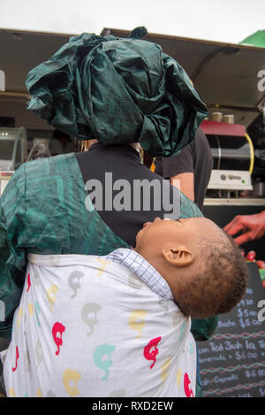 9 Mar 2019, eine Frau in der Linie Kaffee mit ihrem schlafenden Baby auf dem Rücken kaufen am Africultures Festival Wyatt Park, Lidcombe, Sydney Australien. Stockfoto