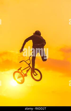 Junger Mann machen Tricks in einem Sprung auf seinem BMX Bike. Sonnenuntergang Silhouette mit Hintergrundbeleuchtung Stockfoto