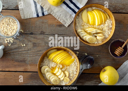 Gesundes Frühstück auf Holz- Hintergrund. Haferflocken mit Obst (Äpfel, Bananen) und Honig Ansicht von oben. Im rustikalen Stil Stockfoto