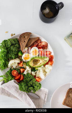 Platte für gesunde Ernährung, Frühstück oder Mittagessen Ansicht von oben. Kohl Kohl, Eier, Avocado, Speck, Tomaten, Rosenkohl, Blumenkohl Brot Toast auf Weiß b Stockfoto